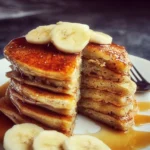 Fluffy homemade banana pancakes served with syrup and fresh bananas