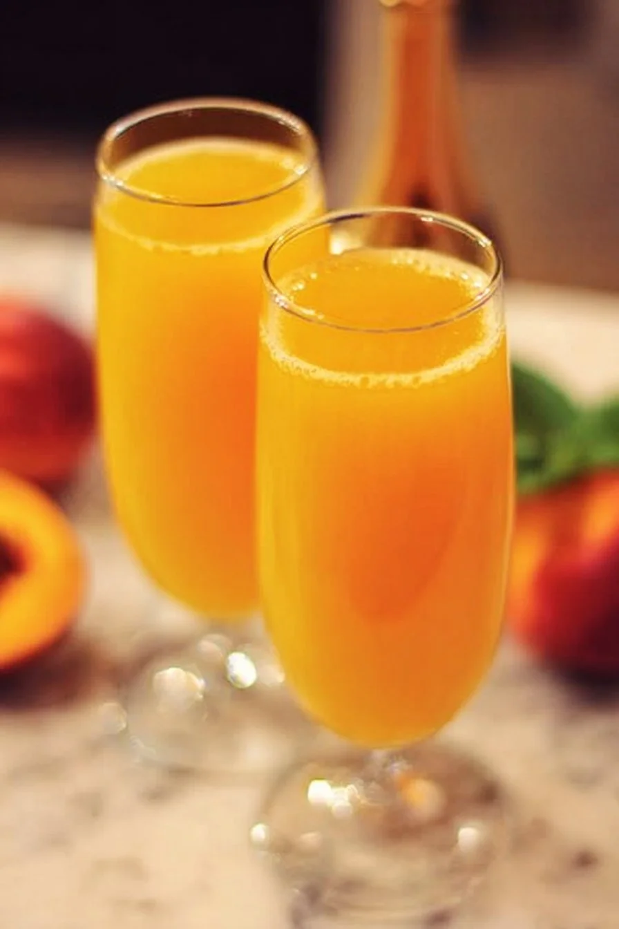 A refreshing glass of peach mimosas served at a brunch table with fruit garnish.
